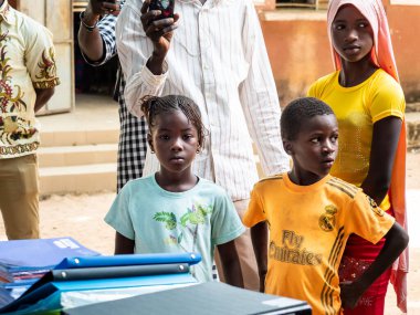 Bour, Senegal - Aralık 2020 civarı. Kimliği belirsiz bir grup genç, güneşli bir yaz gününde okulun bahçesinde ayakta dikiliyorlar. Uluslararası NGO 'nun yeni çantalarını bekliyoruz. Zavallı kırsal çocuklar..