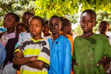 Bour, Senegal - Aralık 2020 civarı. Kimliği belirsiz bir grup genç, güneşli bir yaz gününde okulun bahçesinde ayakta dikiliyorlar. Uluslararası NGO 'nun yeni çantalarını bekliyoruz. Üzgün ve zavallı çocuklar..