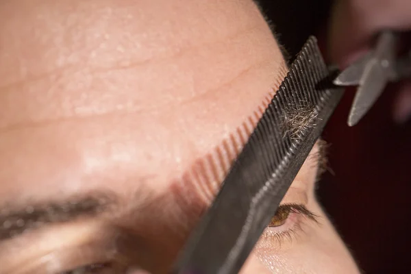 Portrait of man cutting eyebrow hairs.