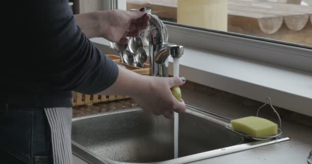 Las manos de la mujer abren el grifo con agua fría y lavan a fondo la manzana hermosa, luego la ponen en el plato — Vídeos de Stock