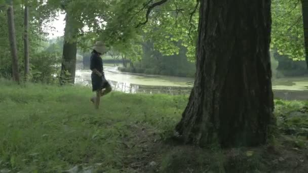 Žena v klobouku u jezera v parku — Stock video