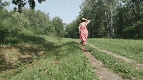 Задний вид молодой женщины в шляпе, бегущей по тропинке, замедленная съемка — стоковое видео