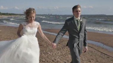 Çift düğünden sonra sahilde romantik gelin ve groomthe çift elele, deniz kenarında kamera hareketi yürümek.