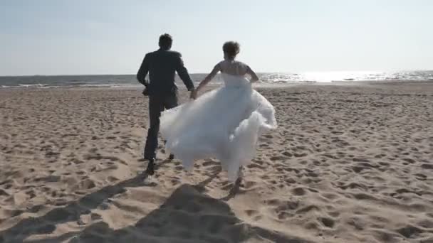 Couple holding hands running on the beach, camera movement — Stock Video