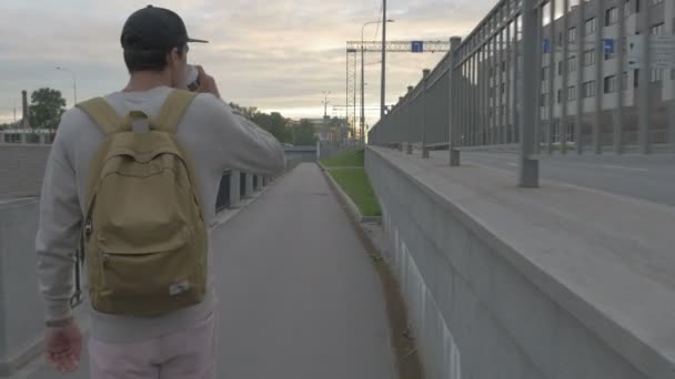 Mladý muž jezdí na skateboardu s kávou v ruce v městě — Stock video
