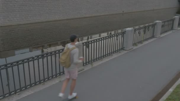 Un jeune homme fait du skateboard avec du café à la main dans la ville — Video