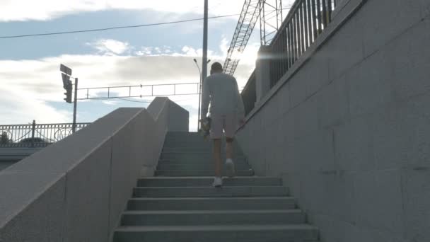 The skateboarder goes up the stairs on the street with a skateboard in hand. — Stock Video