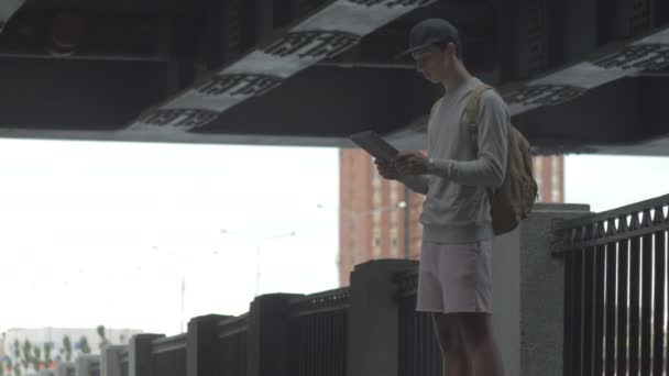 Giovane ragazzo in città su uno skateboard con un tablet in mano in estate — Video Stock