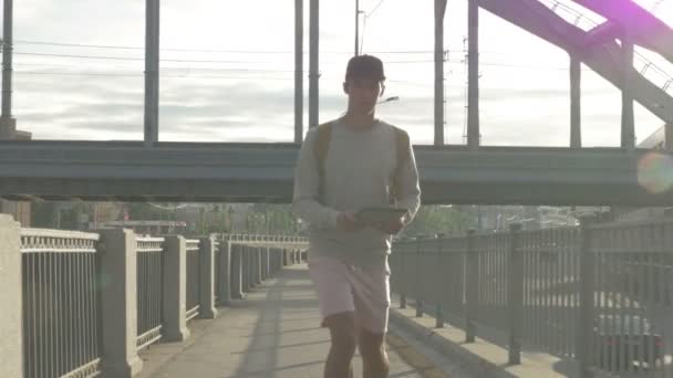 Jonge kerel in de stad op een skateboard met een tablet in de hand in de zomer — Stockvideo