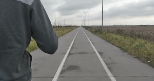 Un hombre en zapatillas corre en el asfalto fuera de la ciudad . — Vídeos de Stock