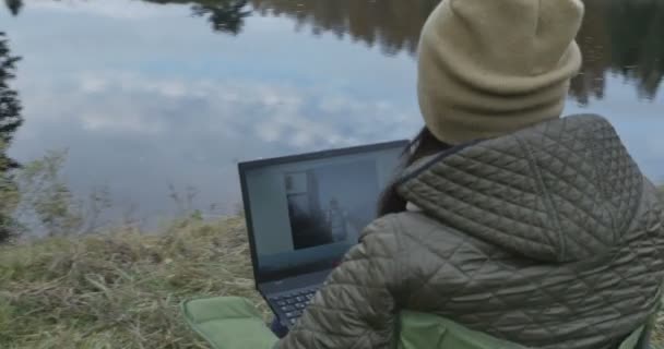 Молодая брюнетка студентка работает на природе на ноутбуке. Осенний день и женщина, наслаждающаяся им при помощи ноутбука . — стоковое видео