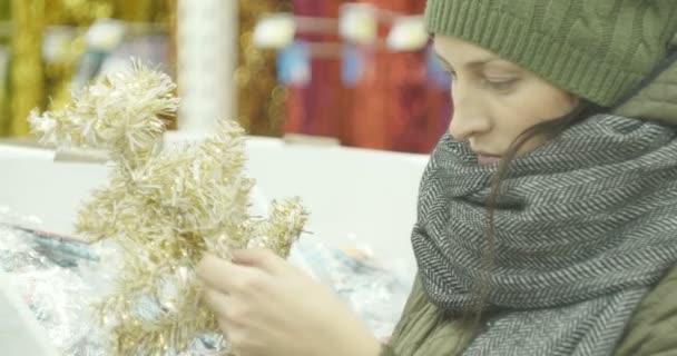 Año nuevo víspera, chica en la tienda elige decoraciones de Navidad, juguetes, bolas, conos . — Vídeos de Stock