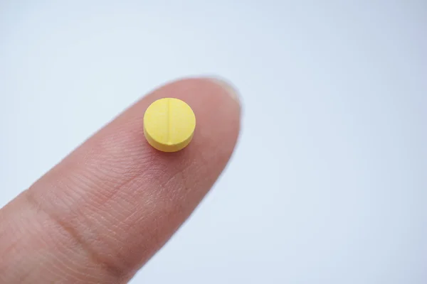 Желтая таблетка на пальце — стоковое фото