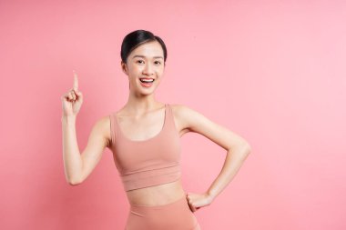 Pembe bir zemine karşı atletik giyinen neşeli bir kadın yukarı doğru poz verir.