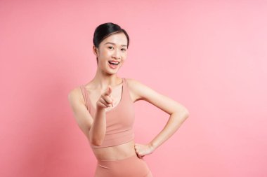 Eşleşen atletik kıyafet giymiş kadın kameraya bakıyor pembe arka planda gülümsüyor.