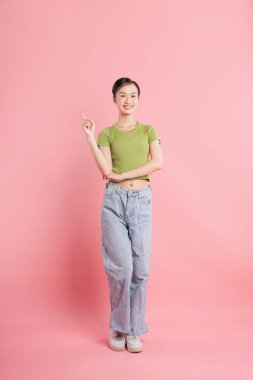 Yeşil bir bluz ve pembeyi gösteren kot pantolon giyen üst sınıf gülüşlü genç bir kadın.