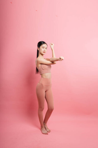 Young woman in athletic wear stretching on solid pink background Health and wellness focus Peaceful
