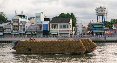 Nehir boyunca ilerleyen samanlarla dolu bir mavna manzarası binaları ve su kulesi olan bir kasabanın yakınında.