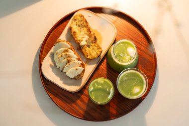 Kahvaltının yukarıdan aşağıya fotoğrafı. Ballı tost ve ahşap tepside yeşil meyve suyu.