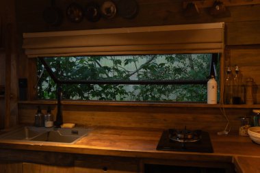 Tezgahın üstündeki pencereden doğa manzaralı kırsal ahşap bir mutfak.