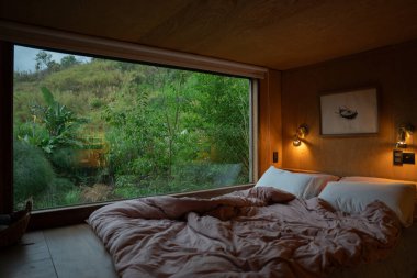 Odanın içi ahşap ve dışarıdaki yeşilliği ve doğal manzarayı gösteren geniş bir penceresi var.