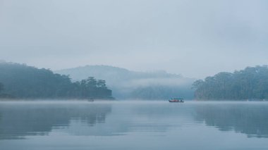 Bir tekne içeren sakin bir göl manzarası ve manzaraya eklenen sisli koşullar