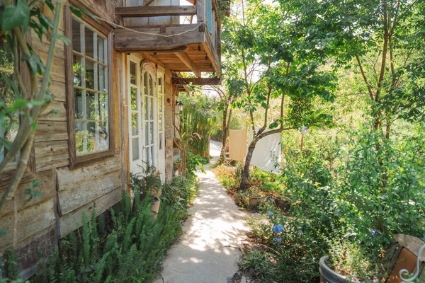 Kırsal bir ahşap evde, geniş bir bahçeye giden patika bir yol yan taraftaki yeşillik çizgisinde asılı.