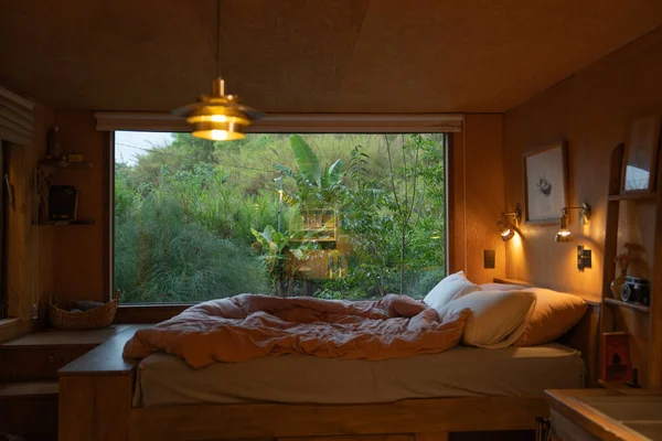 Sıcak ve davetkar bir yatak odası. Geniş bir penceresi var. Yeşil manzaralı.