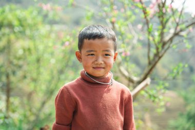 Pas rengi balıkçı yaka kazak giyen genç bir çocuğun yakın plan fotoğrafı. Hmong mücevherleriyle süslenmiş.