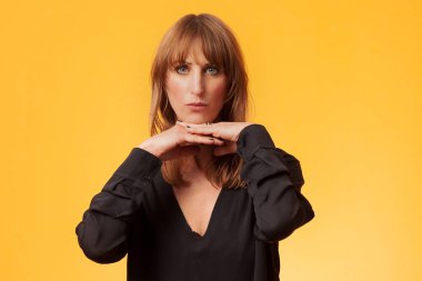 Sarı arka planda siyah bluz giyen çekici bir kadının portresi.