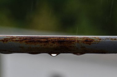A gray railing with rain droplets and rust, terrace view captured with shallow depth for soft, moody backdrop.