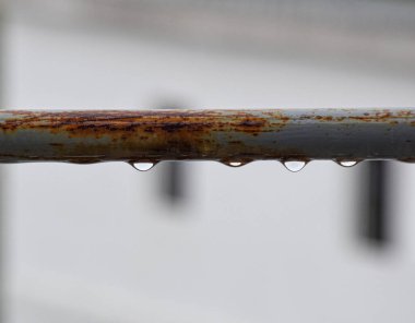 Artistic view of corroded horizontal gray bar on terrace with fresh rain droplets, background intentionally blurred