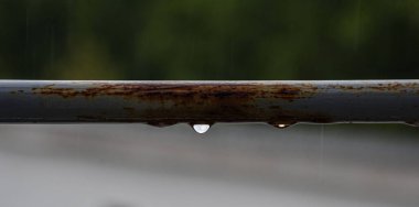 Detailed view of rain droplets on a weathered gray metal bar, terrace railing, with a gently blurred background.