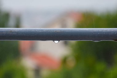 Water droplets on a metal railing bar, rust beginning to show, background blurred to convey rainy weather atmosphere.