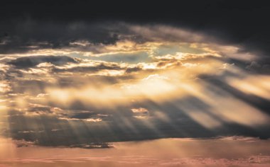 Warm rays from the setting sun shine behind clouds, coloring the sky with magic in this ethereal twilight scene.