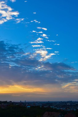 Uyanık şehrin üstündeki katmanlı bulutları aşan yumuşak güneş ışığı, sabah gökyüzünde hafif bir sıcaklık ve renk bırakıyor..