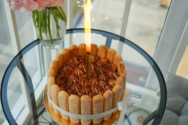 照明付きキャンドルで誕生日のマスターによって自宅でティラミスケーキを調理し 花とクッキーを振りかけたスポンジケーキチョコレートチップ — ストック写真