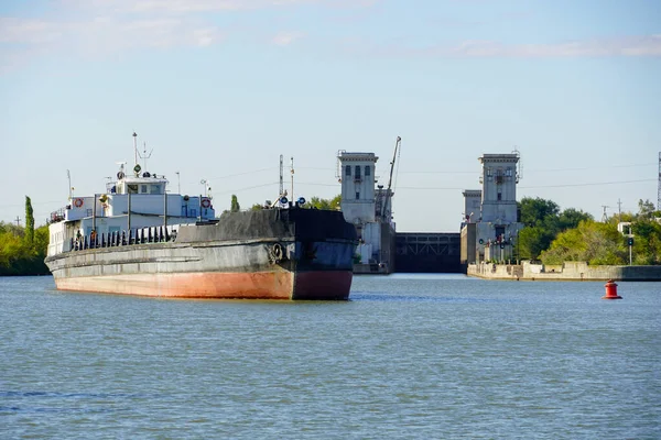Cargo transportation by water transport. An old dry-cargo ship goes along the Volga-Don Shipping Canal against the background of the open chamber of the Volgograd lock. Russia