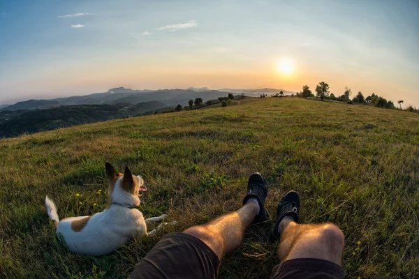 旅行者と彼の犬が草の中に座って、太陽を見て — ストック写真