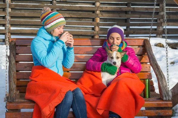 Due giovani donne sorseggiando caffè caldo in una sedia a dondolo in legno su — Foto Stock