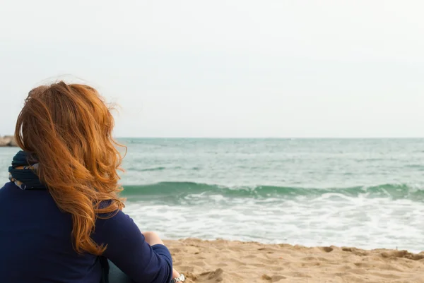 Roodharige meisje op een Barcelona zand strand kijken naar de zee — Stockfoto