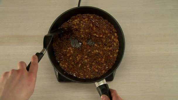 Вид на повара помешивает бобы и мясо во время приготовления пищи — стоковое видео