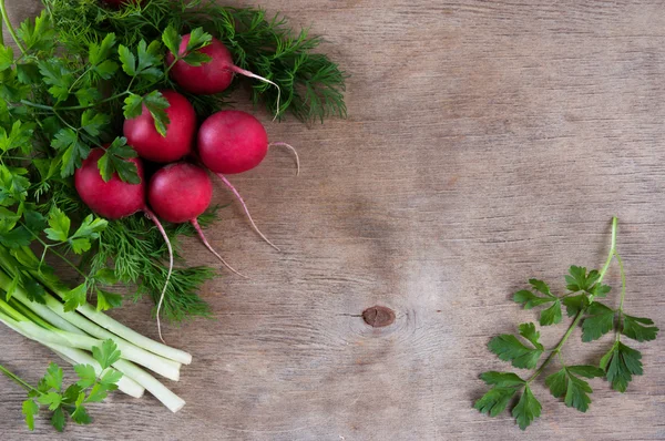 Fresh bundle of red radish with green leaves of dill and parsley on a wooden background