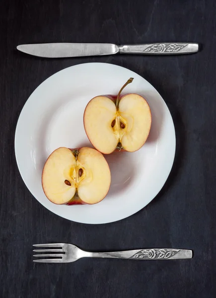 Bıçak ve çatal karanlık bir arka plan üzerinde beyaz bir plaka üzerinde elma. 