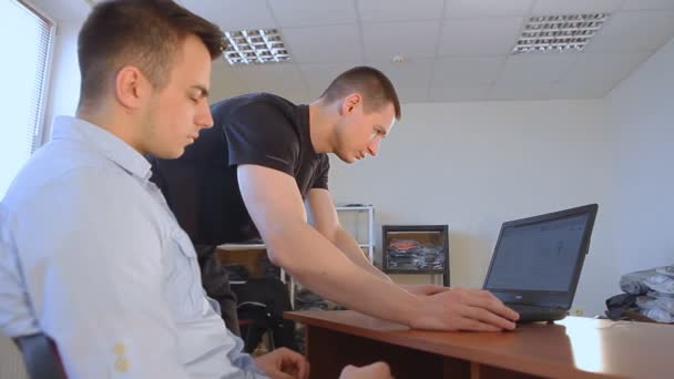 Δύο νέους επιχειρηματίες συζητώντας ένα επιχειρηματικό σχέδιο σε έναν φορητό υπολογιστή στο γραφείο — Αρχείο Βίντεο