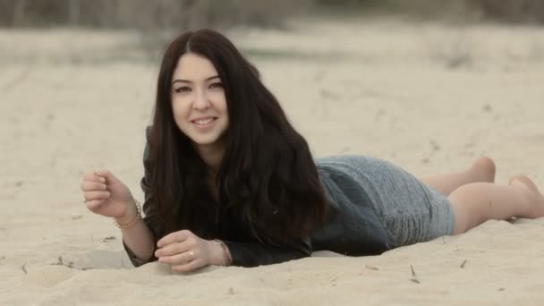 Morena bonito encontra-se na areia e contornos emoções — Vídeo de Stock