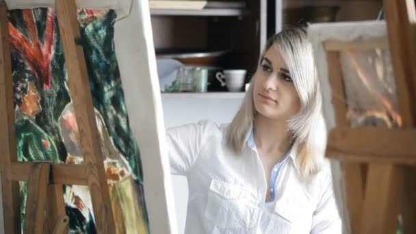 Blonde painter draws paints on an easel — Stock Video