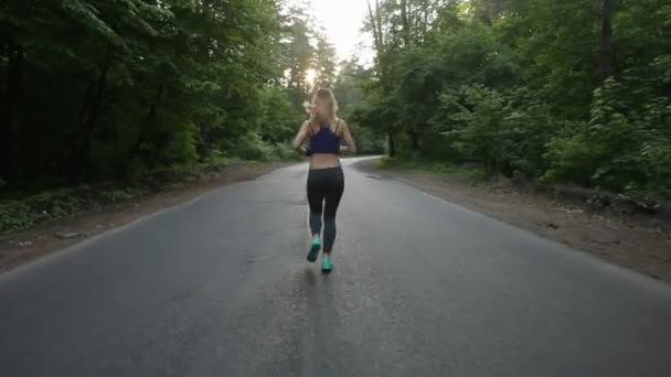Atletisk flicka kör på vägen i skogen. utomhus fitness. Sköt med steadicam — Stockvideo