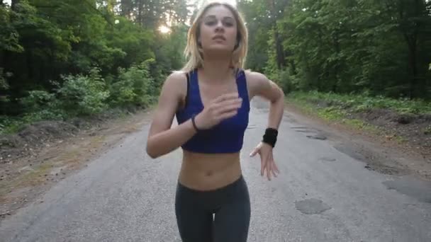 Primer plano de la mujer atlética corriendo por la carretera en el bosque. Disparo con steadicam — Vídeo de stock