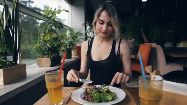 Atractiva mujer en vestido negro en la cafetería come ensalada — Vídeos de Stock